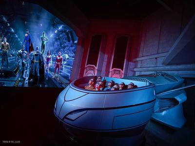 Persone sedute in una capsula futuristica guardano uno schermo con figure in una stanza buia.