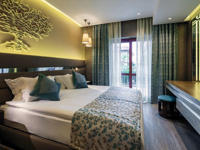 Modernes Schlafzimmer mit Doppelbett, dekorativen Kissen, grünlich-blauen Vorhängen und Holzmöbeln.