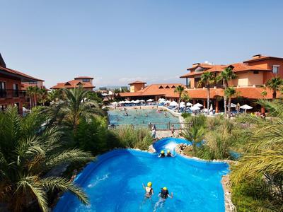 Große Ferienanlage mit Pool, Palmen und roten Dächern unter klarem Himmel.