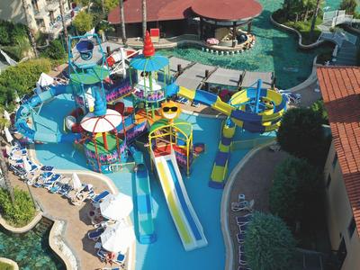 Bunter Wasserpark mit Rutschen, Spielgeräten und mehreren Regenschirmen in sonniger Umgebung.