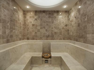 Innenraum einer dampfigen Sauna mit hellen Steinwänden und Sitzbänken aus Marmor.