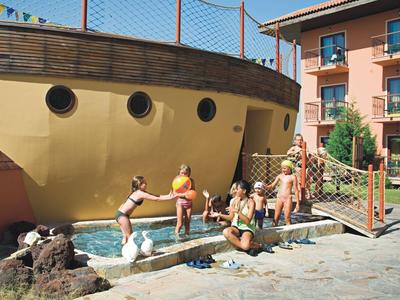 Kinder spielen am Brunnen mit hölzernem Schiffsaufbau in sonnigem Innenhof.