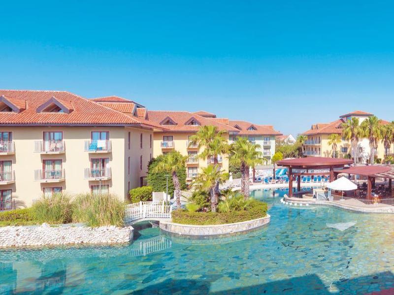 Großes Resort mit Pool, Palmen, roten Dächern und bequemen Liegestühlen unter blauem Himmel.