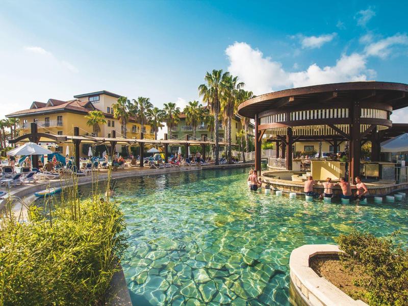 Großer Hotelpool mit klarem Wasser, Palmen und rundem Pavillon in sonniger Urlaubslandschaft.