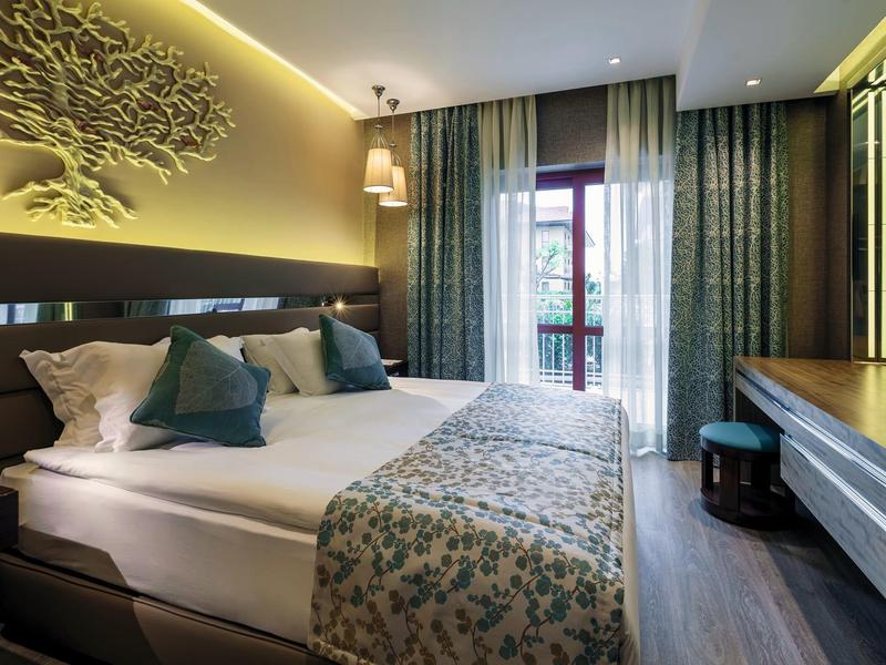 Modernes Schlafzimmer mit Doppelbett, dekorativen Kissen, grünlich-blauen Vorhängen und Holzmöbeln.