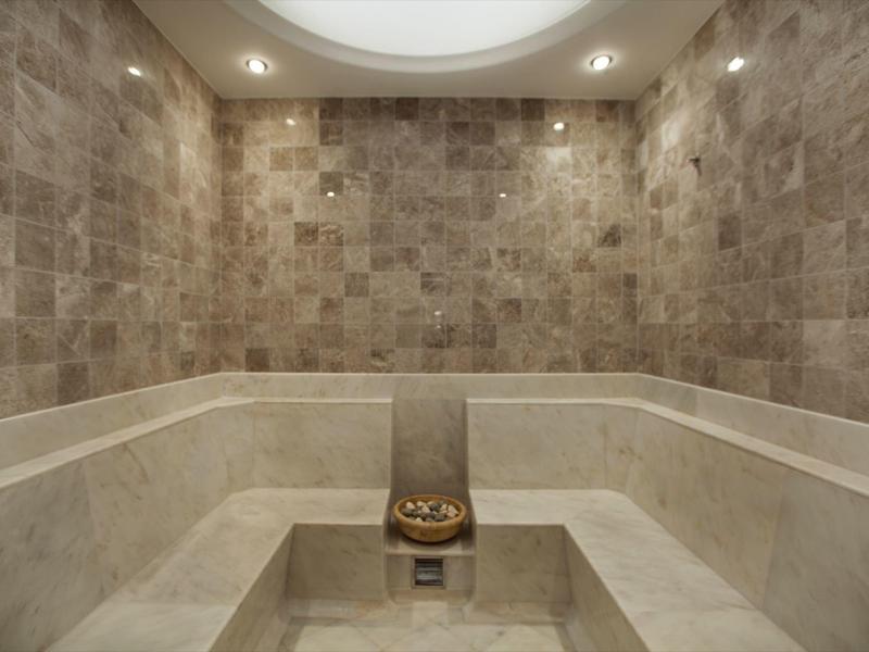 Innenraum einer dampfigen Sauna mit hellen Steinwänden und Sitzbänken aus Marmor.