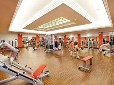 Helles Fitnessstudio mit Holzfußboden, roten Geräten und großem Deckenlicht in modernem Design.