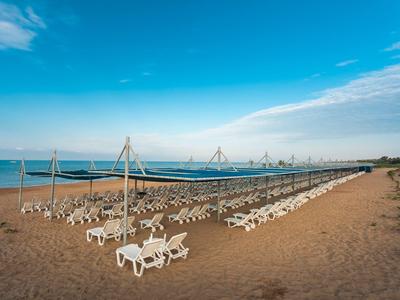 Strand mit vielen weißen Liegestühlen, blauem Himmel und klarem Meer im Hintergrund bei Tageslicht.