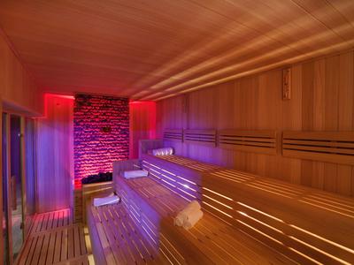 Innenraum einer Sauna mit mehrstufigen Holzliegen und bunter LED-Atmosphärenbeleuchtung.