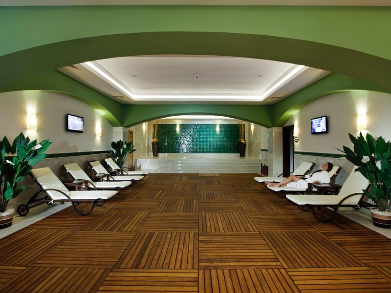 Binnenzwembad met ligstoelen, groene muren en grote planten in potten.