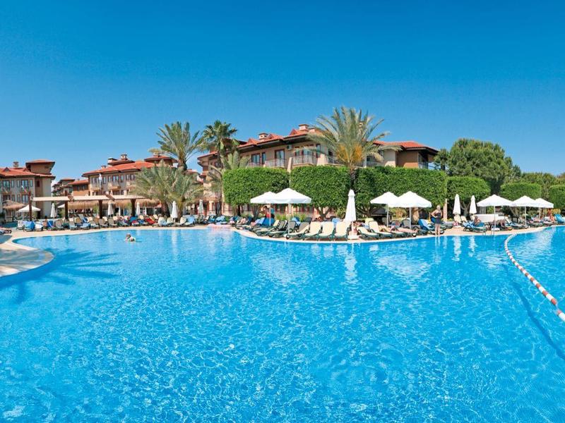 Groot buitenzwembad omgeven door parasols en resortgebouwen onder een heldere hemel.