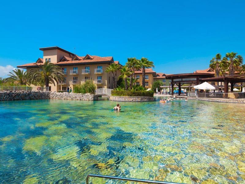 Resort met helderblauw zwembad, palmbomen en ligbedden onder houten pergola's.
