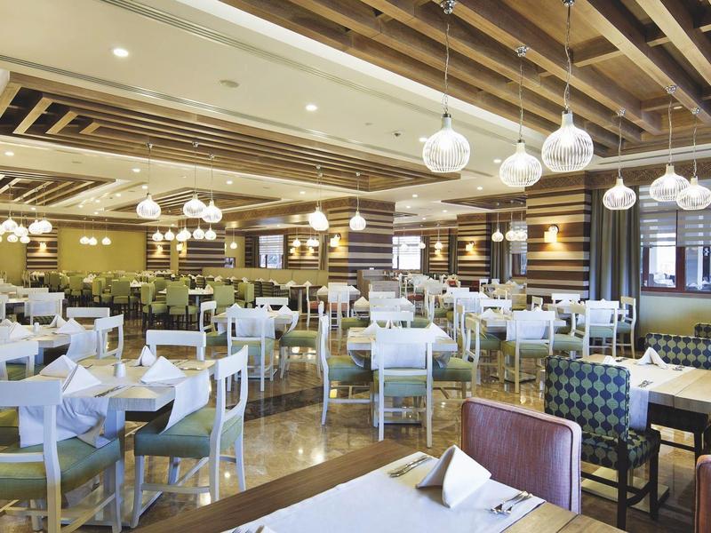 Ruim hotelrestaurant met witte tafels, gestoffeerde stoelen, houten balken en hangende bolvormige lampen.