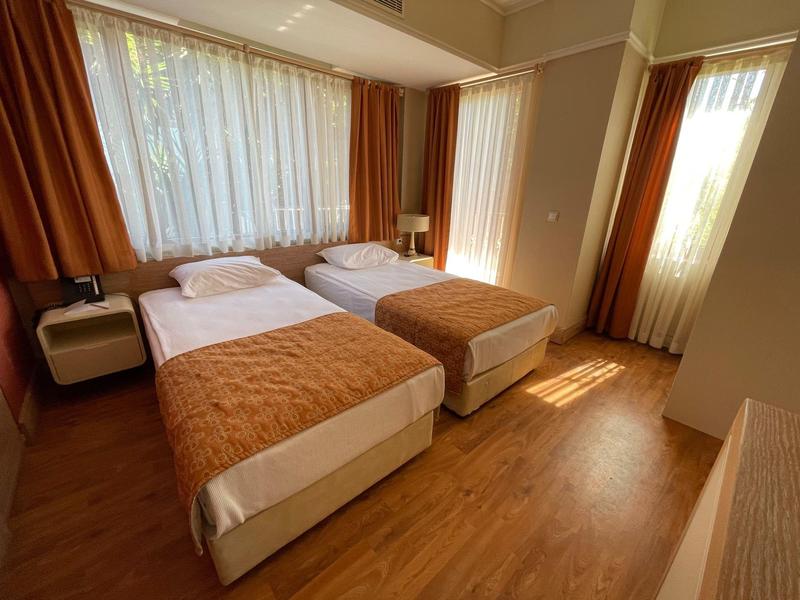 Hotelkamer met twee eenpersoonsbedden, oranje dekbedden, nachtkastjes en grote ramen met gordijnen.