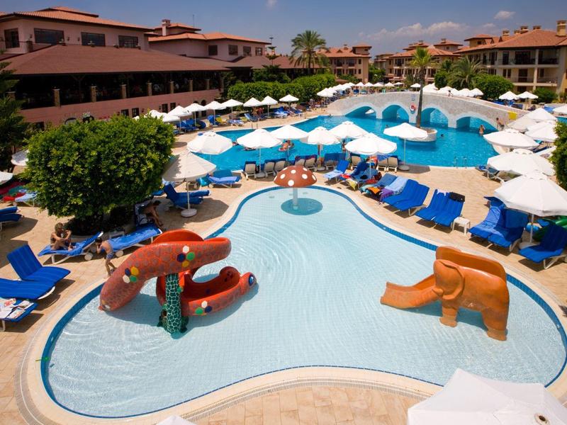 Buitenzwembad met glijbanen omringd door ligstoelen en parasols bij een resort.