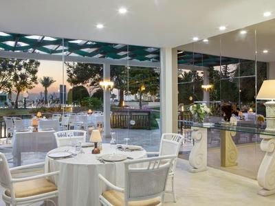 Modernes Restaurant mit weißen Tischen, Stühlen und großem Panoramafenster zum Außenbereich.