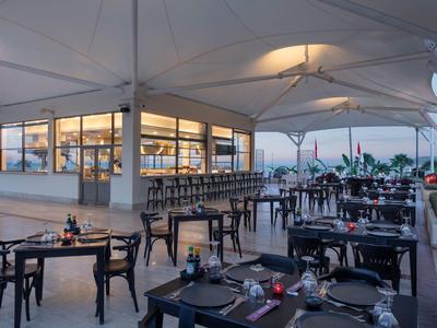 Außerhalb eines modernen Restaurants mit weißem Sonnendach und schwarzen Stühlen auf Terrassenboden.