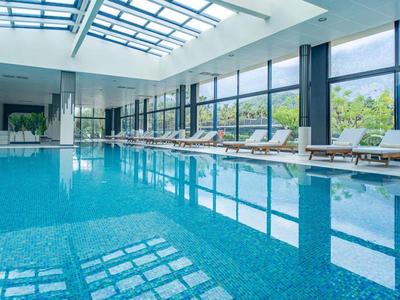 Ein heller Innenpool mit blauen Kacheln, großen Fenstern und Liegestühlen an der Seite.