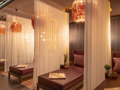 Moderne Wellness-Lounge mit braunen Liegen, sanfter Beleuchtung und halbtransparenten Vorhängen.