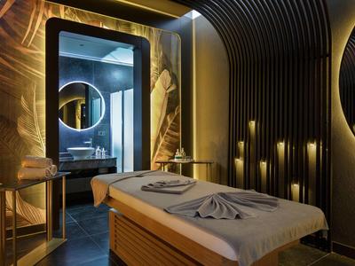 Eleganter Behandlungsraum mit Massagebank, rundem Spiegel, stimmungsvoller Beleuchtung und dunklen Wänden.