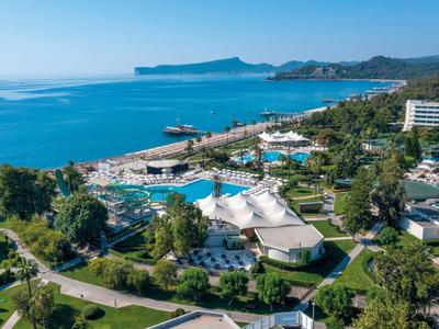 Blick auf eine Küstenanlage mit Pools, grünen Gärten und blauem Meer im Hintergrund unter klarem Himmel.