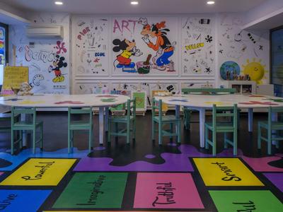 Bunter Klassenraum mit gemalten Figuren, kleinen Tischen, Stühlen und lehrreichem Bodenmuster.