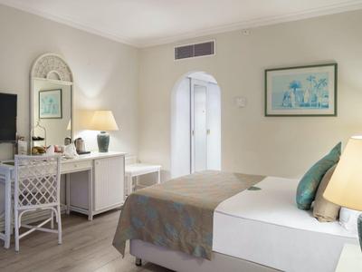 Helles Schlafzimmer mit Doppelbett, Nachttischlampen, Flachbildschirm und Kommode mit Spiegel.