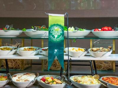 Buffet mit verschiedenen frischen Salaten und Gemüse in weißen Schalen auf zweistufiger Ablage.