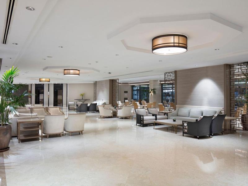 Großer heller Lounge-Bereich mit bequemen Sesseln, Tischen, Pflanzen und deckenleuchten.