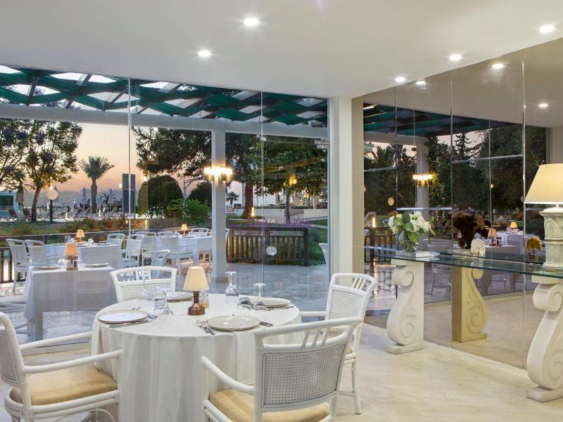 Modernes Restaurant mit weißen Tischen, Stühlen und großem Panoramafenster zum Außenbereich.