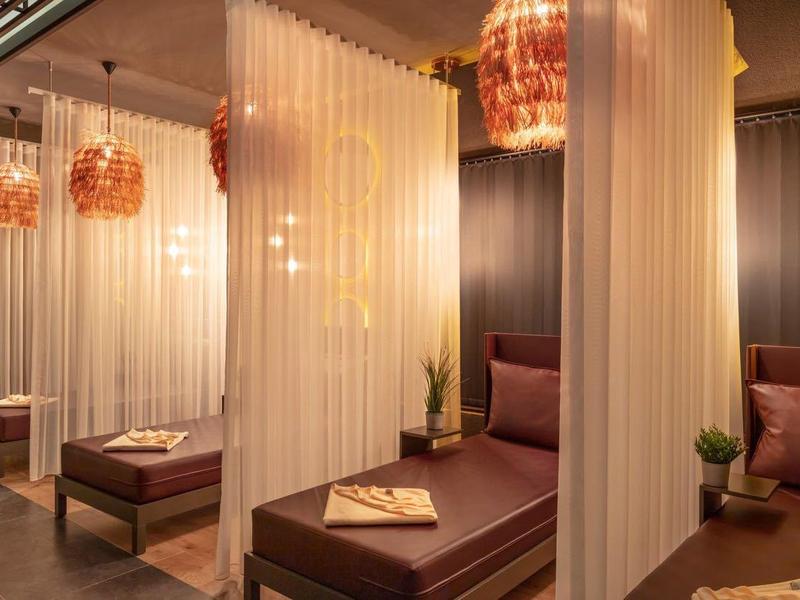 Moderne Wellness-Lounge mit braunen Liegen, sanfter Beleuchtung und halbtransparenten Vorhängen.