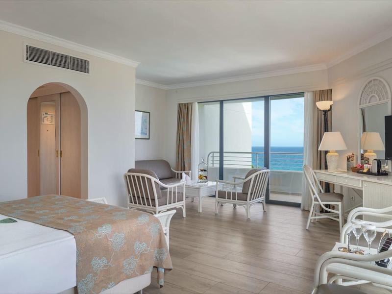 Helles, großzügiges Wohnzimmer mit weißen Möbeln, Holzboden und großem Fenster mit Meerblick.