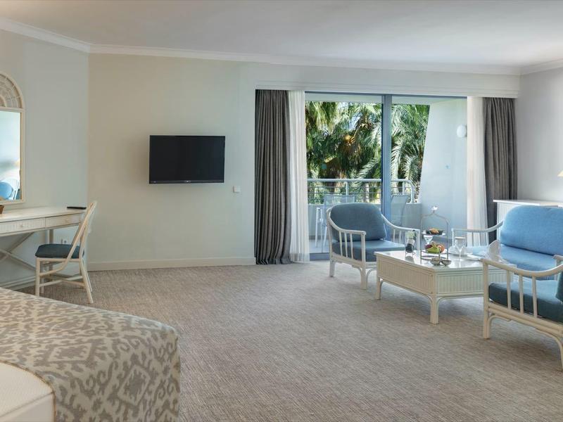 Großes, helles Wohnzimmer mit Teppichboden, weißen Möbeln, blauen Sesseln und Blick auf Garten.