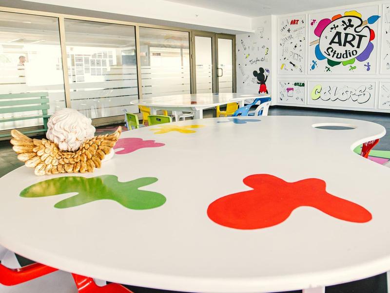 Großer weißer Tisch in Kunstraum mit bunten Farbflecken und Skulptur aus Muscheln darauf.