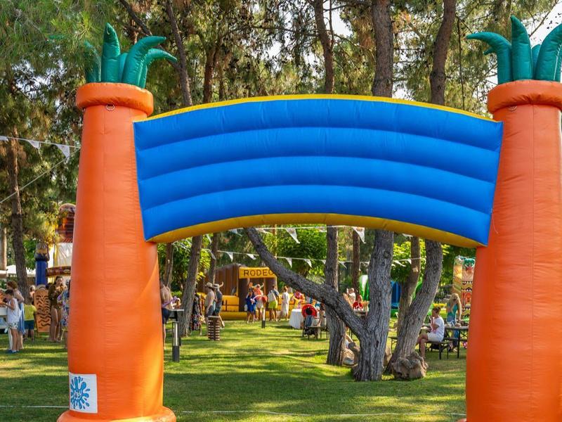 Aufblasbare Karotten mit blauem Bogen auf grasbewachsenem Gelände im Park mit Bäumen.