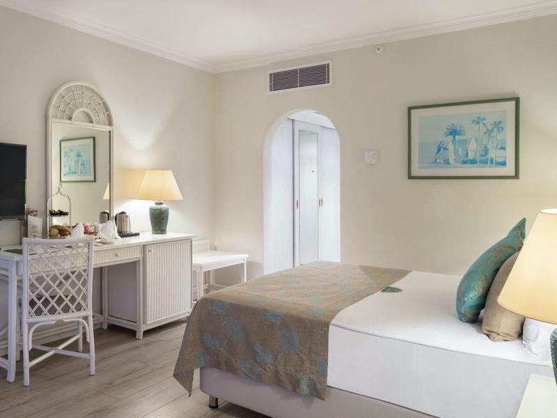 Helles Schlafzimmer mit Doppelbett, Nachttischlampen, Flachbildschirm und Kommode mit Spiegel.