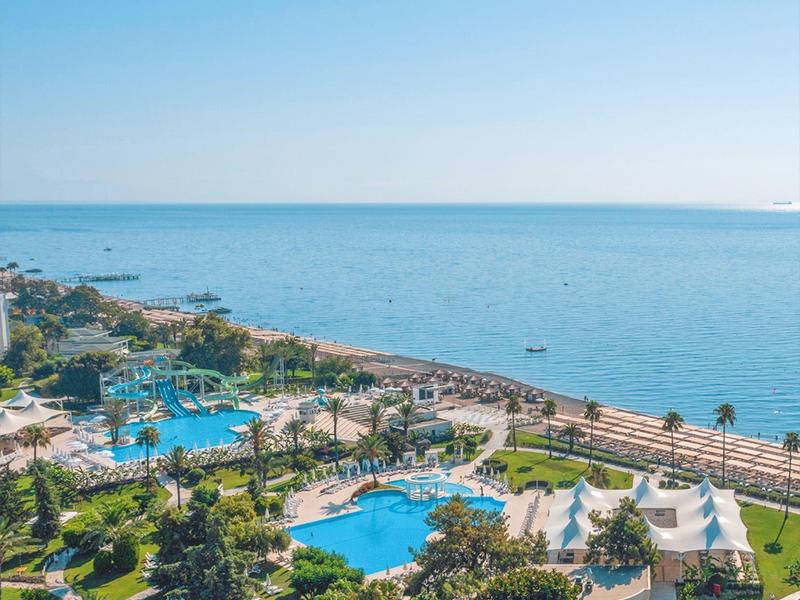 Landschaft mit Hotelanlagen, Pools, grünen Palmen und weiter Sicht auf ruhiges, blaues Meer.