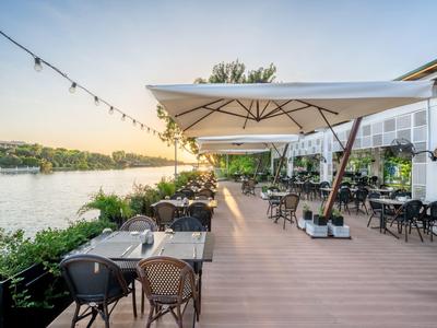 Terrasse d'hôtel avec tables et chaises au bord de l'eau au coucher du soleil.