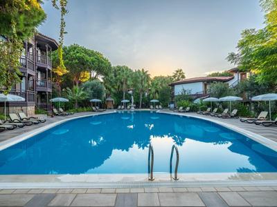 Piscine extérieure d'un hôtel avec chaises longues et environnement verdoyant au coucher du soleil.
