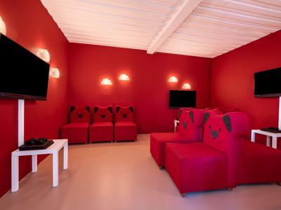 Pièce confortable avec canapés rouges, téléviseurs et tables blanches, idéale pour se détendre.