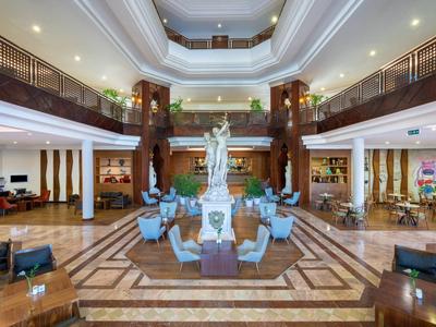 Grand hall d'hôtel avec statue centrale, espaces de sièges et galerie à plusieurs niveaux.