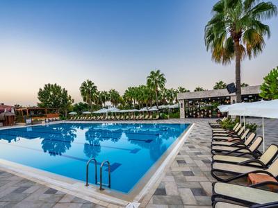 Une grande piscine entourée de chaises longues, de palmiers et d'une végétation dense au coucher du soleil.
