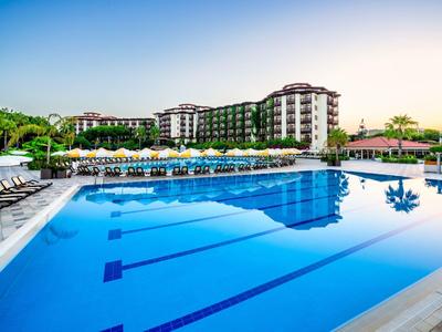 Grande piscine extérieure devant un hôtel à plusieurs étages avec chaises longues et parasols.