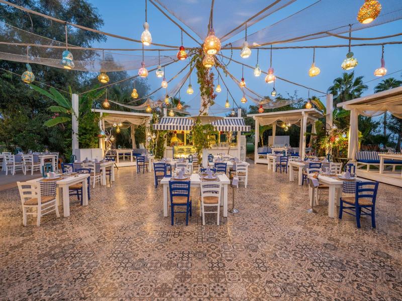 Restaurant en plein air avec tables et chaises éclairées par des guirlandes lumineuses au crépuscule.