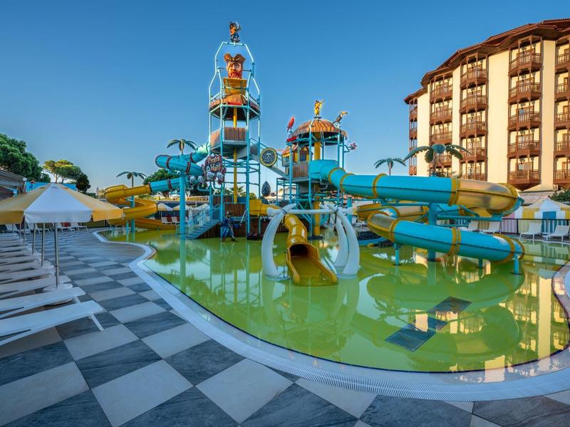 Parc aquatique avec toboggans et jeux d'eau à côté d'un hôtel sous un ciel bleu.