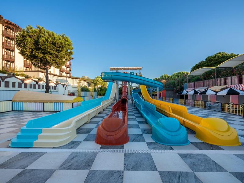 Plusieurs toboggans aquatiques colorés dans une zone de piscine vide d'un hôtel sous un ciel dégagé.
