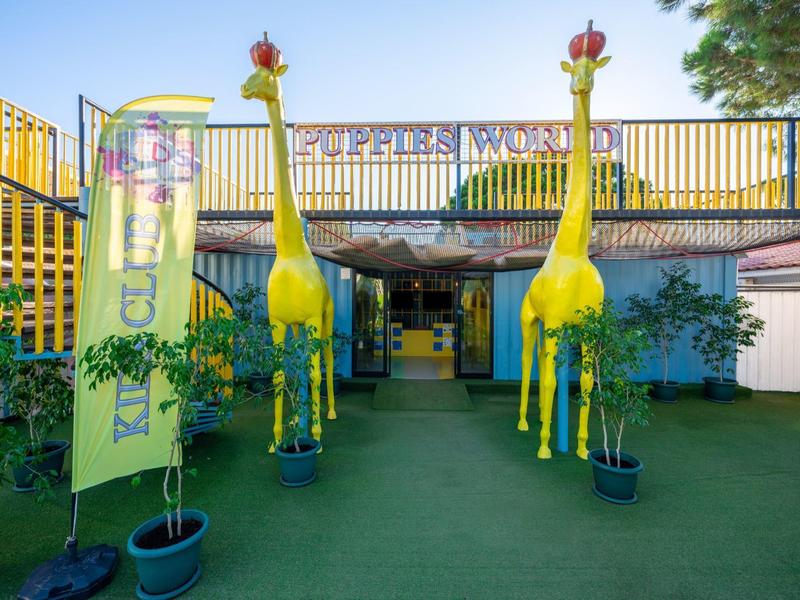 Entrée d'hôtel avec des girafes jaunes colorées et des plantes sur un sol vert.