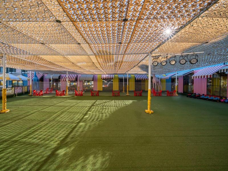 Grand espace extérieur couvert avec sol vert et rideaux colorés.