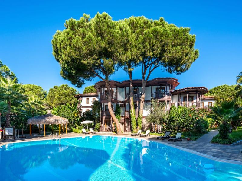 Hôtel avec grande piscine extérieure entourée d'arbres verts et d'un ciel bleu clair.