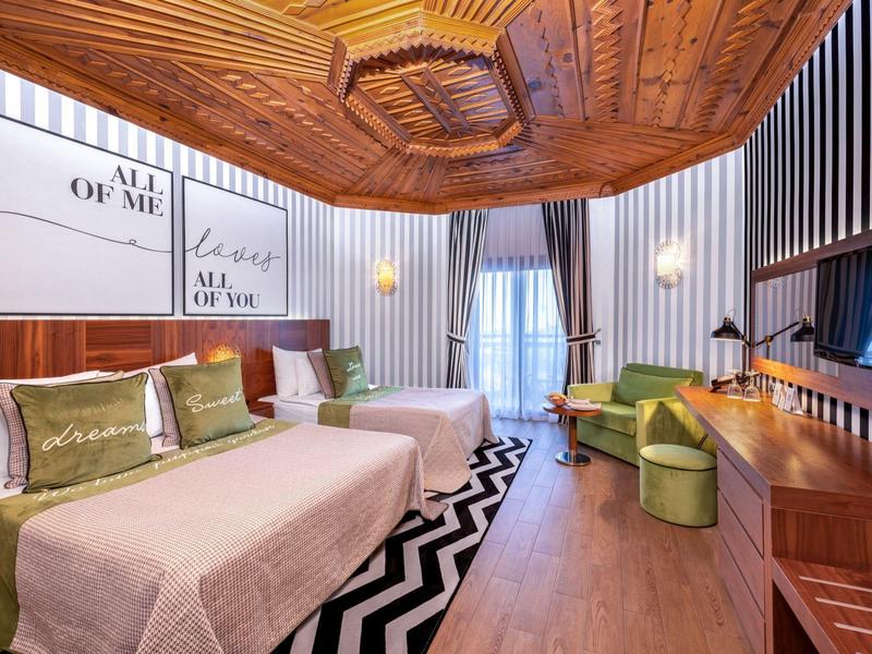 Chambre d'hôtel moderne avec deux lits, plafond en bois et grande fenêtre avec rideaux.